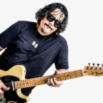 Guitarrista Roberto Lessa de óculos escuros tocando uma guitarra Fender Telecaster amarela com escudo preto