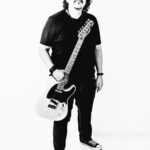 Foto em preto e branco de corpo inteiro do guitarrista Roberto Lessa segurando uma guitarra Fender Telecaster
