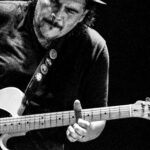 Foto em preto e branco do guitarrista Roberto Lessa usando chapéu e tocando uma guitarra Fender Telecaster